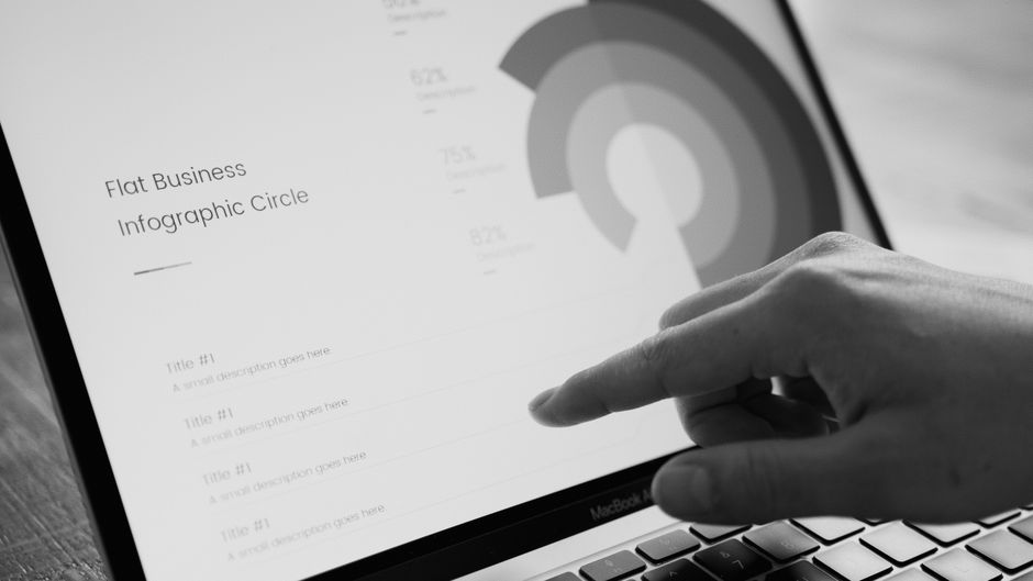 Finger pointing at a business infographic circle on a laptop screen in grayscale.