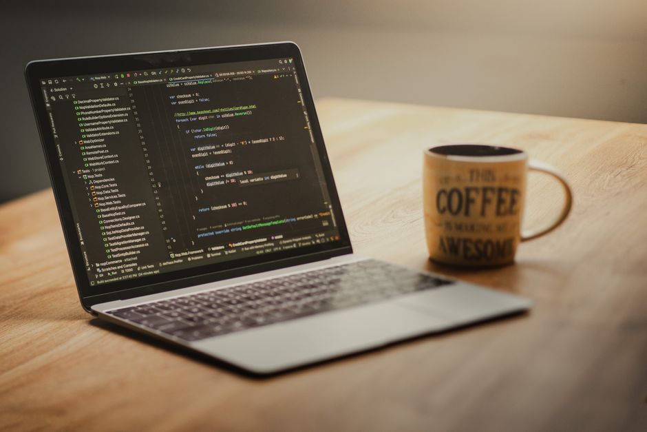 Laptop displaying code editor on a desk with a coffee mug beside it, suggesting a workspace or home office setting.